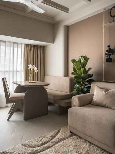 Beige living-dining nook with curved dining table, upholstered sofa, and fiddle leaf fig against terracotta wall