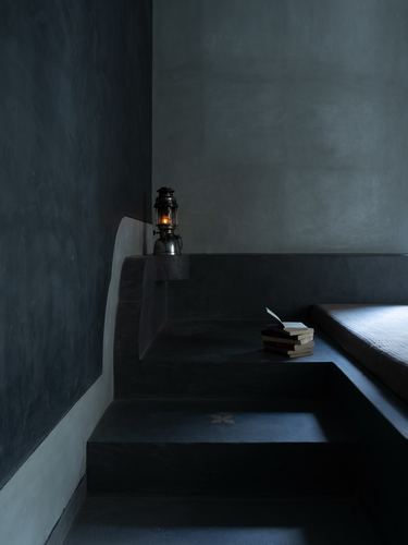 Dark plastered stepped seating platform with lit lantern and stacked books in dim interior
