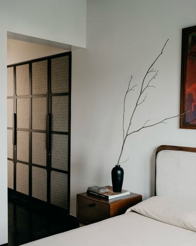 Bedroom corner with cane wardrobe doors, wooden nightstand, and black vase with dried branches