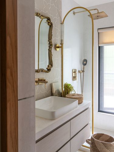Bathroom vanity with vessel sink, antique brass mirror, and arched brass shower frame beside tiled wall