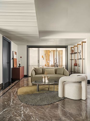 Living room with olive curved sofa, bouclé armchair, round patterned rug on marble floor