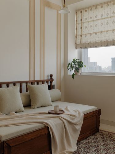 Wooden daybed with cream cushions beneath a paneled wall near a city-view window