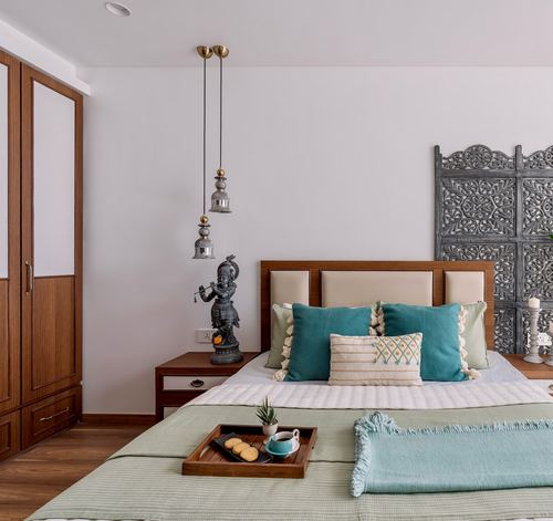 Bedroom with teal cushions, wooden headboard, carved screen backdrop, and hanging brass lanterns