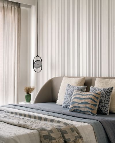 Bedroom corner with fluted wall, curved headboard, blue and cream layered pillows, pendant light