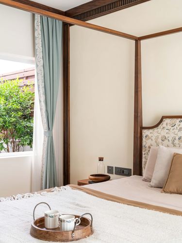 Four-poster wooden bed with floral headboard beside window with sage curtain and breakfast tray