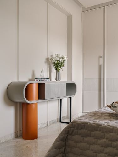 Curved console table with orange cylindrical leg against paneled wall in minimalist bedroom