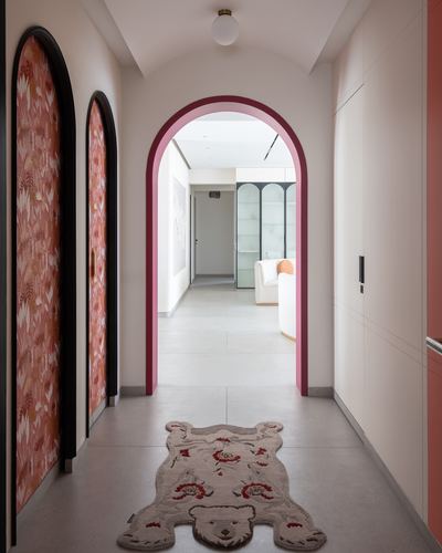 Corridor with arched maroon-framed doorway, floral wallpaper panels, and a bear-shaped rug on stone floor.