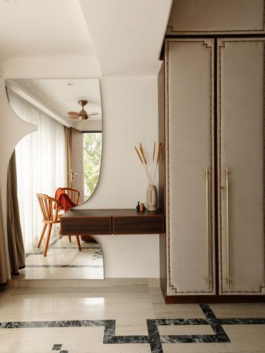 Curved mirror reflecting a bedroom nook beside an upholstered wardrobe with brass handles