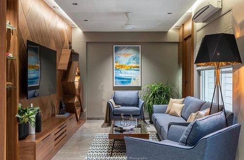 Living room with wood-paneled TV wall, blue sofas, glass coffee table and framed seascape painting