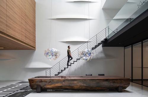 Man walking down a black staircase in a white double-height foyer with crystal pendant lights and a live-edge wood bench