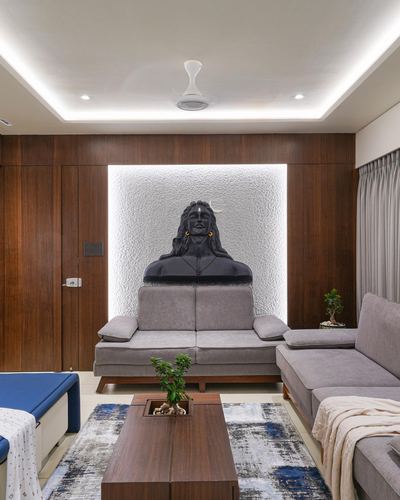 Grey sofas face a wood-panelled wall with a backlit niche holding a dark Shiva bust sculpture