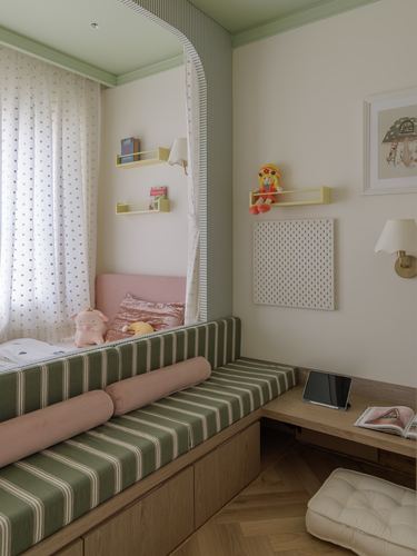 Child's bedroom nook with striped green daybed, pink bolster, canopy curtain, and floating shelves.