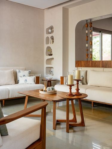 Living room with teak nesting tables, cream sofas, and carved wall niches in Ahmedabad villa