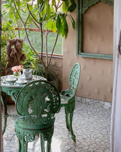 Green cast-iron bistro table and chairs on a balcony with mosaic stone flooring and greenery
