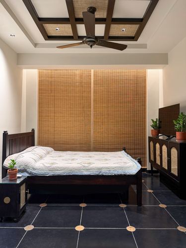 Bedroom with dark wood bed, cane window screens, coffered ceiling and terracotta-inlaid dark stone floor