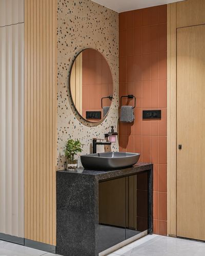 Bathroom vanity with oval mirror on terrazzo wall, black stone counter, terracotta tile