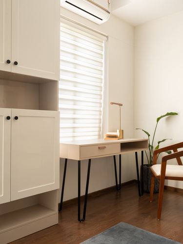 Minimalist study nook with hairpin-leg desk, cabinetry, and armchair by a sheer-curtained window