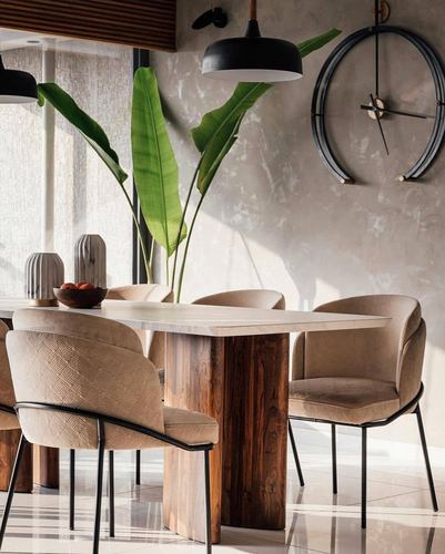 Dining table with stone top and wood base beneath oversized round wall clock and pendant light
