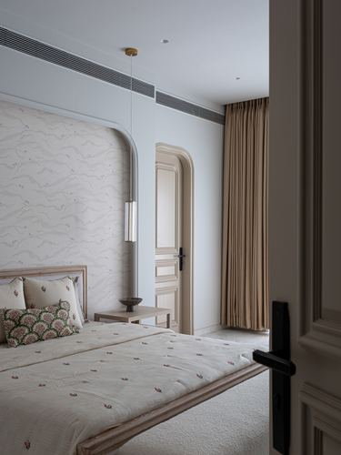 Bedroom with arched textured headboard wall, pendant light, and view through arched door to curtained window