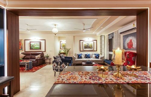 Eclectic Noida living room with layered seating, framed art, and candle-lit foreground table.