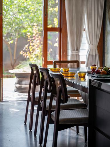 Dining table with cane-back chairs beside open glass doors overlooking greenery