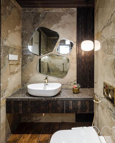 Marble bathroom with three asymmetric mirrors, fluted dark panel, and brass pendant lanterns over a vessel sink