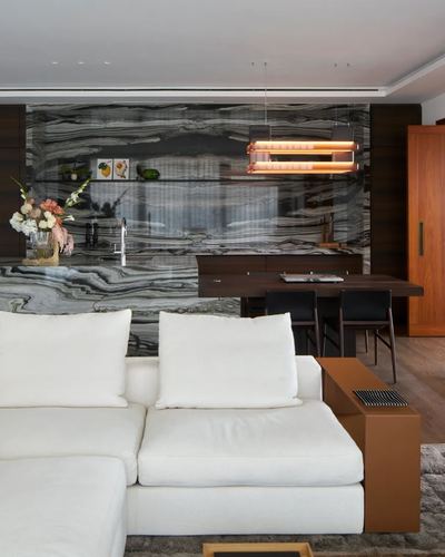 Living room with white sectional facing a dining area backed by a large veined marble wall