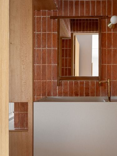 Terracotta-tiled bathroom wall with wood-framed mirror, brass faucet, and exposed timber post
