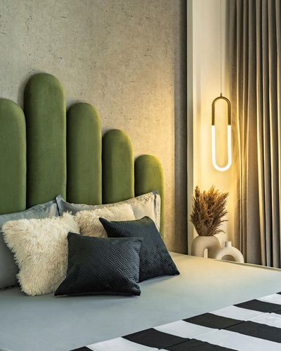 Bed with green scalloped velvet headboard, black and cream pillows, glowing U-shaped pendant light beside curtain.