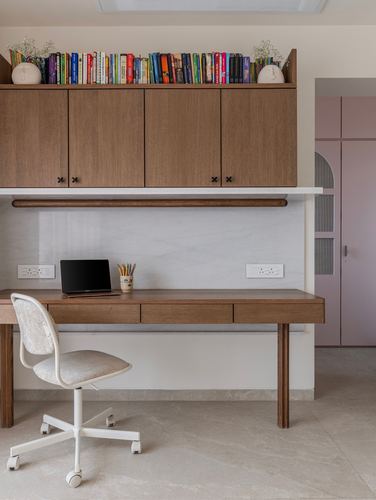 Built-in wooden study desk under overhead cabinets with books, laptop, and a white office chair