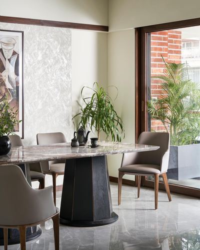 Dining area with oval marble table on sculptural base, taupe chairs, and view to brick facade