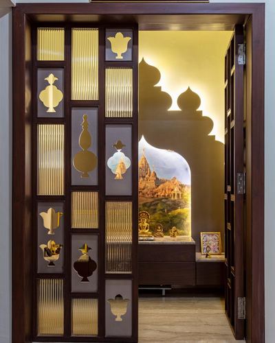 Carved wooden pooja door with brass motifs opening to a backlit arched shrine niche