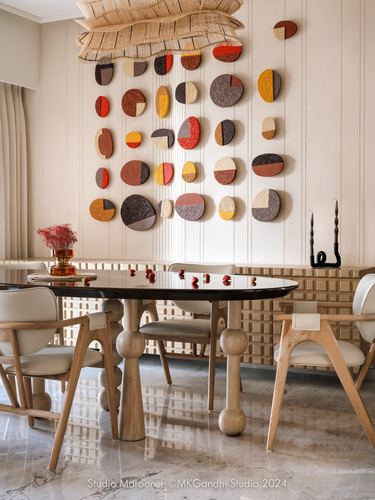 Dining room with oval wood table, cream chairs, and circular sculptural wall art in warm tones