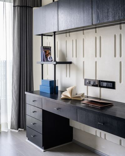 Dark wood study desk with drawers against a ribbed textured plaster wall, floating shelf above