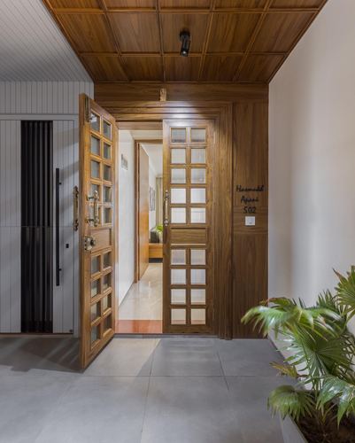 Open wooden glass-paned double door leading into an apartment entrance corridor with tiled floor and plant