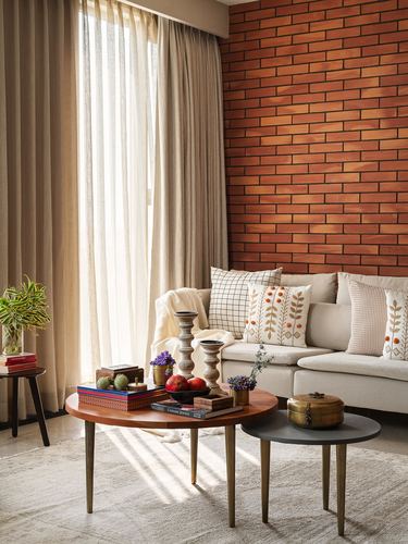 Living room corner with brick wall, beige sofa, and round wood coffee tables in sunlight