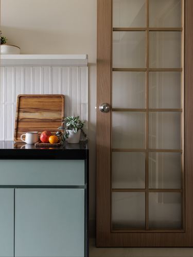 Kitchen corner with sage cabinets, black counter, wooden cutting board and glazed timber door