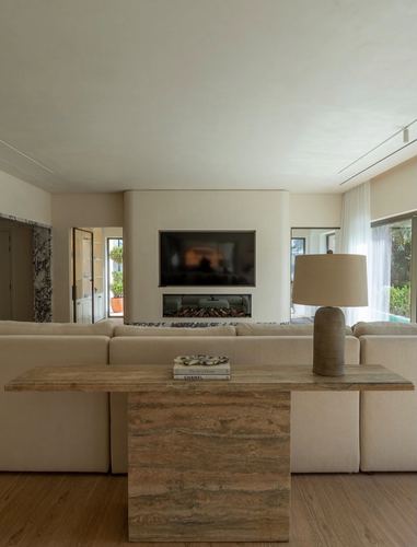 Neutral living room with travertine console behind sofa facing a recessed fireplace and mounted tv