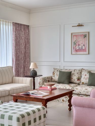 Living room with floral sofa, pink armchair, checkered ottoman, and framed art on paneled wall