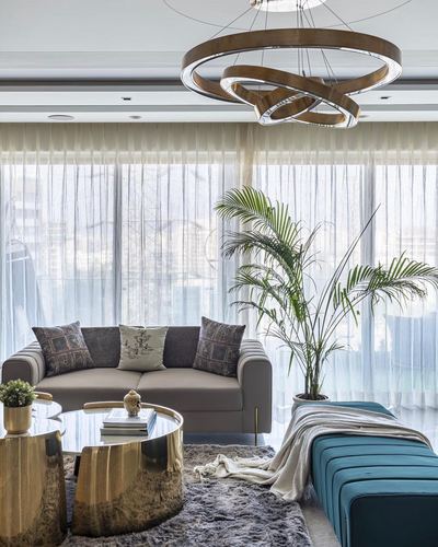 Living room with sheer curtains, brass ring pendant, gray sofa, brass coffee table and teal bench