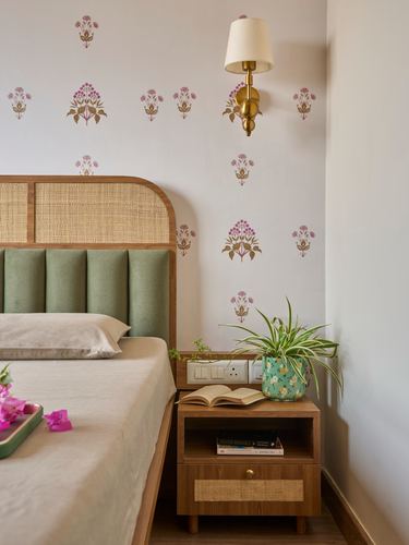 Bedroom corner with cane headboard, green channel-tufted panel, wooden nightstand and floral wallpaper