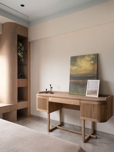 Wooden console table with fluted drawers and framed art beside a curved wood shelving unit in a bedroom