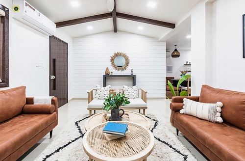 Living room with tan leather sofas, cane tables, jute rug, and shiplap wall under vaulted beamed ceiling
