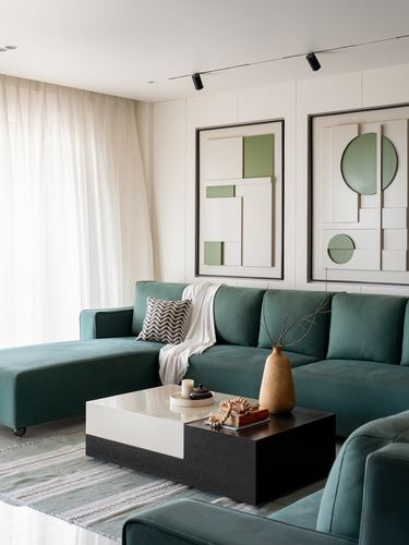 Teal velvet sectional sofa facing two-tone coffee table beneath sculptural green and cream wall art