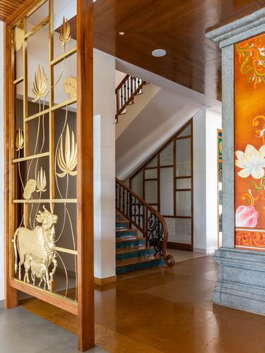 Foyer with brass cow jali screen, wooden staircase, and painted mural pillar in Tamil Nadu home