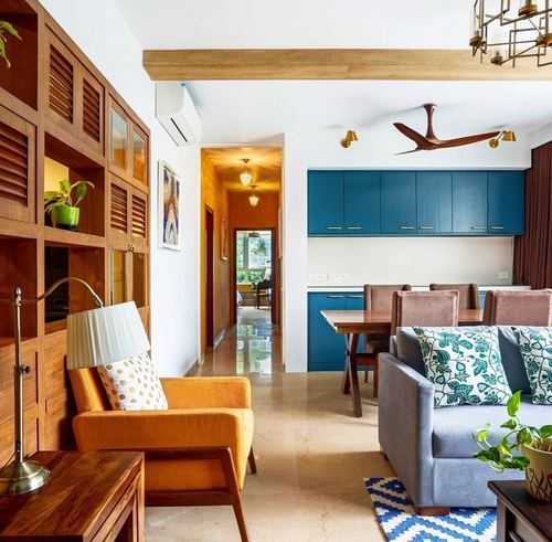 Open living room with orange armchair, grey sofa, teal kitchen cabinets and wooden louvered unit
