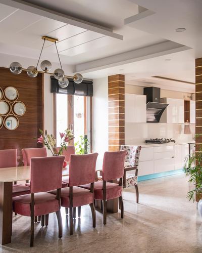 Dining room with pink velvet chairs, brass chandelier, and open kitchen beyond