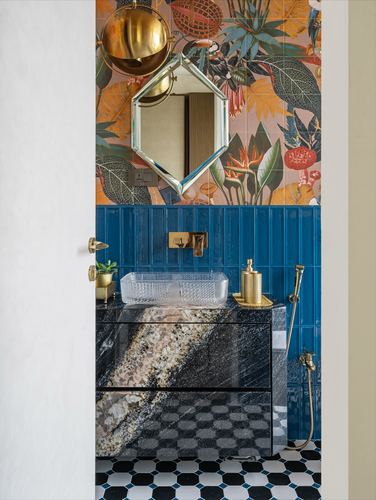 Bathroom seen through doorway with floral tile, blue ribbed tile, and stone vanity with brass fittings