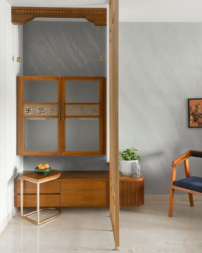 Wooden pooja unit with fluted glass doors and om motifs beside a living area with armchair