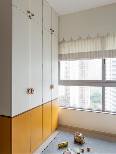 Children's bedroom with mustard and white wardrobe, striped scalloped curtains, and toy-covered play mat near window